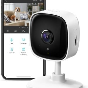 White security camera in front of a smartphone displaying live footage of a dog sitting on a couch.