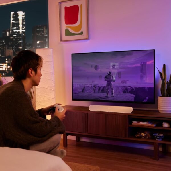 Person playing a video game on a TV in a cozy, modern apartment at night with a city skyline visible through the window.