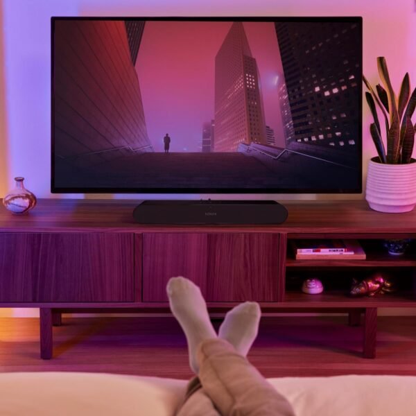 Person's feet resting on a bed, watching TV in a cozy living room with ambient lighting and a wooden TV stand.