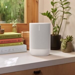 White Sonos speaker on a countertop with plants and books in the background.